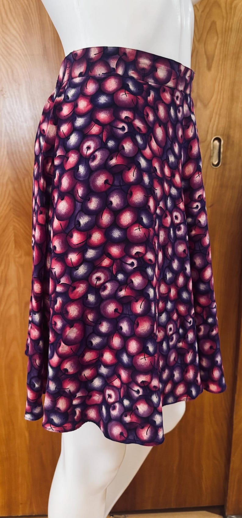 Peut inclure: Jupe trap&egrave;ze orn&eacute;e d'un motif de cerises vives dans les tons de violet, rose et blanc. La jupe est faite d'un tissu fluide et a une taille haute. La jupe mesure environ 61 cm de long.