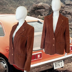 Könnte beinhalten: Ein brauner Cordblazer mit zwei Knöpfen und zwei Taschen. Der Blazer befindet sich auf einem Mannequin und der Hintergrund ist ein orangefarbenes Oldtimer-Auto mit dem Jahr 1977 auf dem Nummernschild.