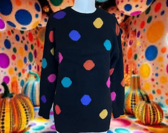May include: Black sweater with large, colorful polka dots in yellow, blue, orange, pink, and teal. The sweater is displayed on a mannequin. The background features a colorful, polka-dotted design.