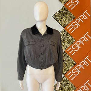 May include: A gray cropped jacket with a black velvet collar and button-up front. The jacket has two small pockets and long sleeves. The jacket is displayed on a mannequin.