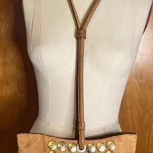 May include: A tan suede tote bag with a long tan leather strap. The bag has a decorative border of silver metal circles.