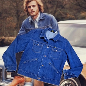 May include: A blue denim jacket with two chest pockets and two side pockets. The jacket has a button-up front and a collar. The Wrangler logo is visible on the jacket. The jacket is a classic style.