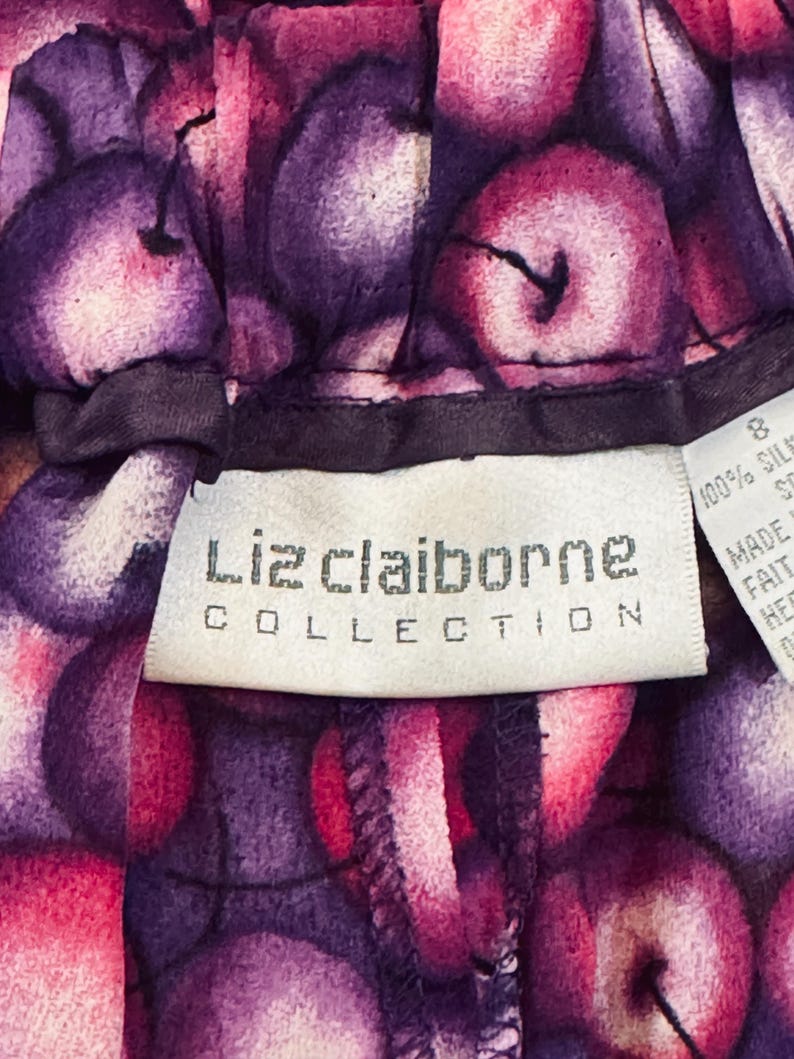 Peut inclure: Gros plan sur un v&ecirc;tement avec un motif vibrant de fruits violets et roses. L'&eacute;tiquette indique "Liz Claiborne Collection". Le tissu semble &ecirc;tre de la soie. Le v&ecirc;tement est de taille 8.