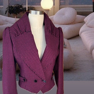 Può includere: Un blazer rosa e nero a quadri, corto, con chiusura a doppio petto e un grande colletto.