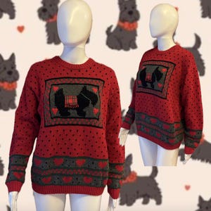 May include: Red knit sweater featuring a Scottish Terrier design. The sweater has a crew neck, long sleeves, and a pattern of small black hearts. The design includes a framed image of two terriers with a plaid blanket, and a gray and red heart border.