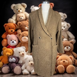 Peut inclure: Un long manteau marron à double boutonnage, avec un col châle et deux poches. Le manteau est fait d'un tissu pelucheux et texturé.