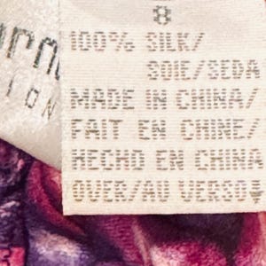 Peut inclure: Gros plan sur une &eacute;tiquette blanche avec le chiffre 8 imprim&eacute;. L'&eacute;tiquette indique "100% SILK" et "MADE IN CHINA" en anglais, fran&ccedil;ais et espagnol. L'&eacute;tiquette est attach&eacute;e &agrave; un tissu floral violet et rose.