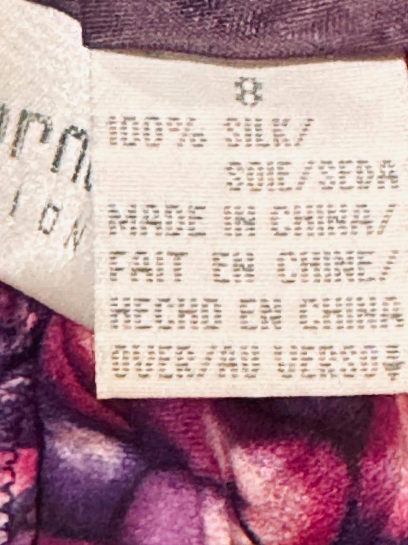 Peut inclure: Gros plan sur une &eacute;tiquette blanche avec le chiffre 8 imprim&eacute;. L'&eacute;tiquette indique "100% SILK" et "MADE IN CHINA" en anglais, fran&ccedil;ais et espagnol. L'&eacute;tiquette est attach&eacute;e &agrave; un tissu floral violet et rose.