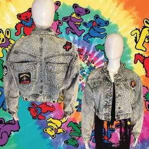 Peut inclure: Une veste en jean bleu clair avec des patchs d'ours de bande dessinée. La veste est courte et a un devant boutonné.