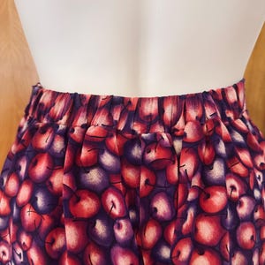 Peut inclure: Un pantalon taille haute avec un imprim&eacute; de cerises. Le tissu pr&eacute;sente un motif de cerises rouges et violettes avec des tiges vertes sur un fond violet fonc&eacute;. La taille est &eacute;lastique.
