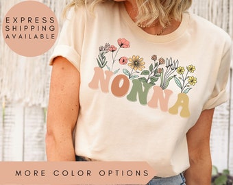 May include: A light beige t-shirt with a floral design and the word "NONNA" in colorful letters.