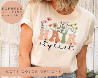 May include: A light beige t-shirt with a floral design and the text "Hair stylist" in a retro font.