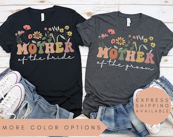 May include: Two t-shirts with a floral design and the text "Mother of the bride" and "Mother of the groom" in colorful letters. The shirts are black and dark grey heather.