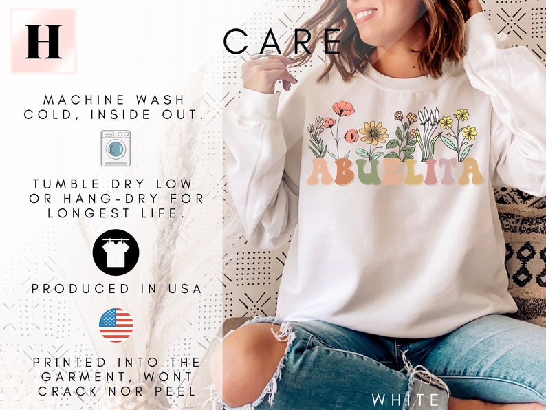 May include: White sweatshirt with a floral design and the text "Abuelita" in colorful letters. The sweatshirt is shown on a model wearing blue jeans. The text "CARE" is in black letters at the top of the image. The text "MACHINE WASH COLD, INSIDE OUT." is in black letters. The text "TUMBLE DRY LOW OR HANG-DRY FOR LONGEST LIFE." is in black letters. The text "PRODUCED IN USA" is in black letters. The text "PRINTED INTO THE GARMENT, WONT CRACK NOR PEEL" is in black letters. The text "WHITE" is in black letters.