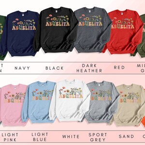 May include: A collection of sweatshirts in various colors featuring the text "Abuelita" with a floral design. The colors include forest green, navy, black, dark heather, red, military green, ash, light pink, light blue, white, sport grey, sand, and orange.