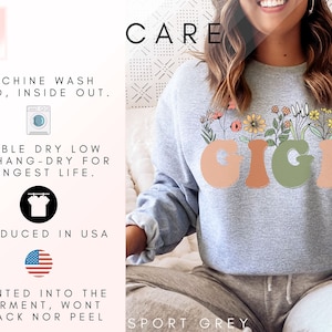 May include: A gray sweatshirt with the word "GIGI" printed in a colorful, retro font with flowers growing out of the letters. The text "CARE" is printed in black at the top of the image. The text "SPORT GREY" is printed at the bottom of the image. The text "MACHINE WASH COLD, INSIDE OUT. TUMBLE DRY LOW OR HANG-DRY FOR LONGEST LIFE. PRODUCED IN USA PRINTED INTO THE GARMENT, WONT CRACK NOR PEEL" is printed on the left side of the image.