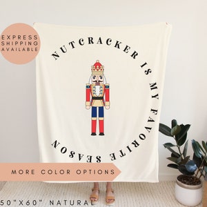 May include: White fleece blanket with a red and blue nutcracker illustration and the text "Nutcracker is my favorite season".
