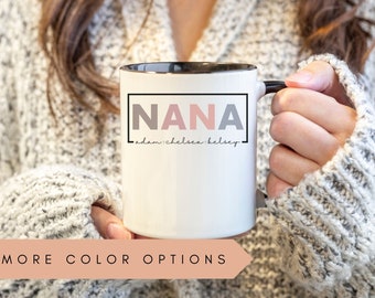 May include: White ceramic mug with a black rim and handle. The mug has a black rectangle with the word "NANA" in pink, gray, and white letters. Below the rectangle is the text "adam, chelsea, kelsey".