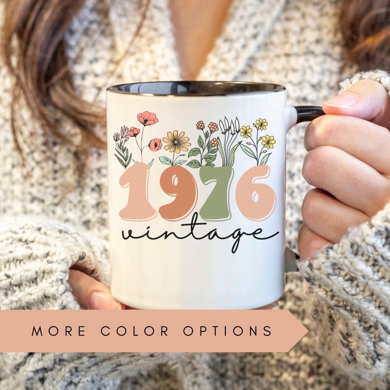 A person is holding a mug with the text "1976 Vintage" printed on it, surrounded by colorful floral designs.