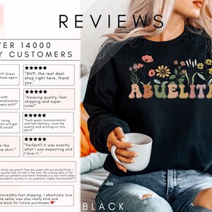 May include: Black sweatshirt with a floral design and the text "ABUELITA" in colorful letters. The sweatshirt is being worn by a person holding a white mug.