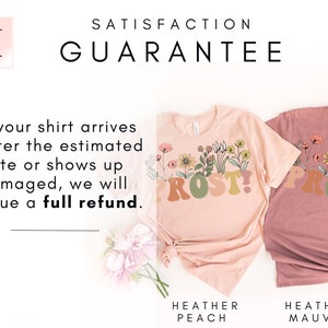 K&ouml;nnte beinhalten: Zwei T-Shirts mit dem Aufdruck "PROST!" Die Shirts sind in den Farben Heidelbeer-Pfirsich und Heidelbeer-Lila. Der Text ist von einem floralen Design umgeben.