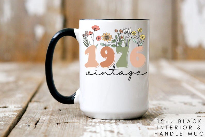 A white mug with a black handle, featuring a floral design and the text "1976 Vintage" printed on it.