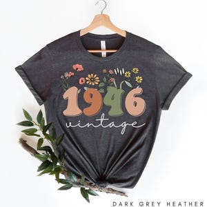 A dark grey t-shirt with a floral design and the text "1946 Vintage" printed on it, hanging on a wooden hanger.