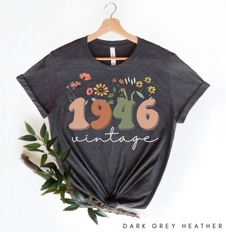 A dark grey t-shirt with a floral design and the text "1946 Vintage" printed on it, hanging on a wooden hanger.