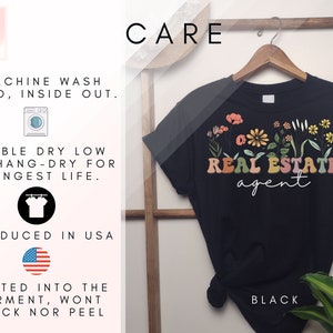 May include: Black t-shirt with a floral design and the text "REAL ESTATE agent". The shirt is on a hanger and has care instructions printed on the left side of the image.