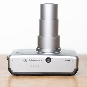 Może przedstawiać: Srebrny aparat fotograficzny Rollei Germany z chowanym obiektywem i numerem seryjnym 7004891.