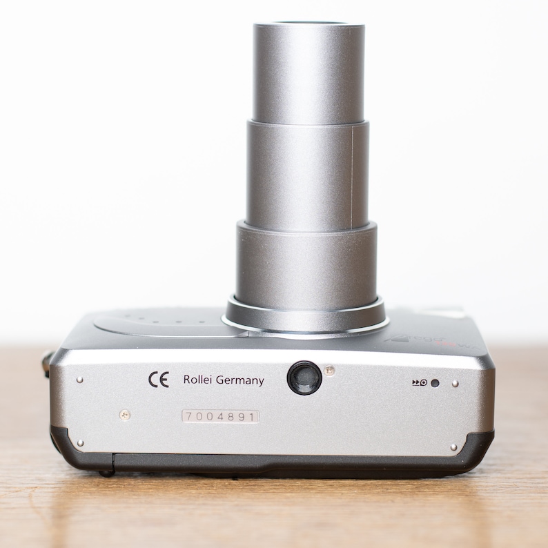 Może przedstawiać: Srebrny aparat fotograficzny Rollei Germany z chowanym obiektywem i numerem seryjnym 7004891.
