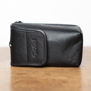 Może przedstawiać: Czarny sk&oacute;rzany futerał na aparat z wytłoczonym napisem "Rollei" z przodu.