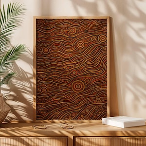 Op de afbeelding: Een ingelijst kunstwerk met een Aboriginal dot painting in bruin-, oranje- en geeltinten. Het abstracte ontwerp heeft een golfachtig patroon met cirkelvormige motieven. De houten lijst vult de warme tonen van het kunstwerk aan.