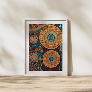 May include: Framed abstract art print with a vibrant dot painting. The artwork displays concentric circles in orange, teal, and brown, forming a captivating design. The print is presented in a white frame, suitable for various interior styles.