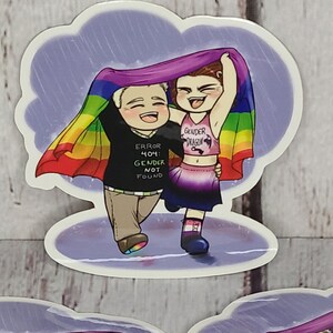 May include: Two cartoon figures, one wearing a black shirt with the text "ERROR 404: GENDER NOT FOUND" and the other wearing a pink tank top with the text "GENDER DRAGON", are holding a rainbow pride flag over their heads while walking in the rain.