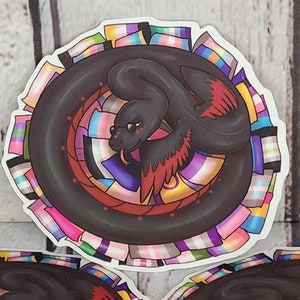 May include: A black snake with red wings curled around a circle of colorful pride flags. The snake has a yellow eye and a pink tongue.