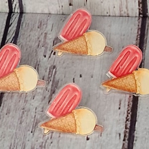 Puede incluir: Cuatro juegos de paletas rojas y conos de helado. Las paletas tienen forma de corazón y los conos de helado son de color amarillo claro con un cono de waffle marrón.
