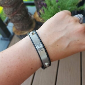 May include: A black leather bracelet with a silver metal plate engraved with the name "MAC".