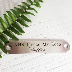 May include: A silver metal tag with the text "NHS L'EGGO MY EGGO "Waffles"" engraved on it.