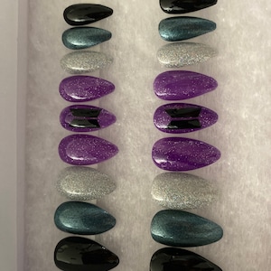 May include: A set of press-on nails in a variety of colors, including black, teal, silver glitter, and purple. Some nails feature a black logo. The nails are arranged in two columns inside a white box.