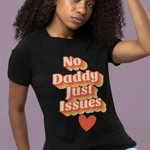 May include: A black t-shirt with a retro-style graphic that reads "No Daddy Just Issues" with a red heart.