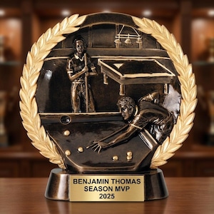 May include: Bronze-colored trophy featuring a detailed relief of a billiards scene, framed by a gold laurel wreath. The trophy base includes a gold plaque with the text "BENJAMIN THOMAS SEASON MVP 2025". The trophy depicts two players and a pool table.