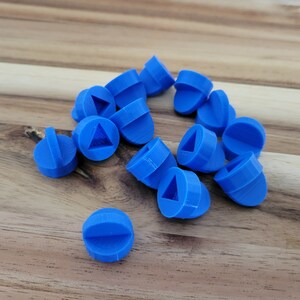 Könnte beinhalten: Eine Gruppe von 14 blauen Spielsteinen aus Kunststoff mit einem Dreieck und einem Halbkreis. Die Steine liegen auf einer Holzoberfläche.