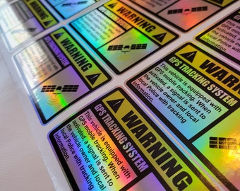 May include: A close-up of several holographic stickers with the text "WARNING GPS TRACKING SYSTEM" and a satellite icon. The stickers are yellow and black with a holographic rainbow effect.