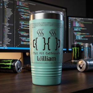 Può includere: Un bicchiere termico turchese con coperchio argentato. Il bicchiere presenta la scritta "Ctrl Alt Caffeinate" e il nome "William" in nero. Il design include codice binario e simboli di tazza di caffè. Lattine di bevande energetiche sullo sfondo.