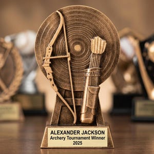 Puede incluir: Trofeo de tiro con arco de bronce con arco y flecha, carcaj de flechas y diana. La base rectangular tiene el texto "ALEXANDER JACKSON Archery Tournament Winner 2025".