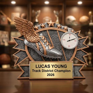 Könnte beinhalten: Leichtathletik-Trophäe mit silbernem Laufschuh, bronzefarbenen Flügeln und Stoppuhr. Die Trophäe hat eine goldene Plakette mit der Aufschrift "LUCAS YOUNG Track District Champion 2026".