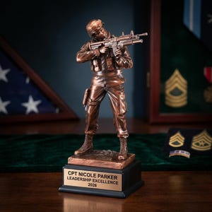 Puede incluir: Figura de soldado de color bronce sosteniendo un rifle, montada sobre una base negra con una placa dorada. La placa dice "CPT NICOLE PARKER LEADERSHIP EXCELLENCE 2026". La figura está detallada con uniforme militar.