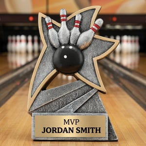May include: A bowling trophy featuring a star-shaped design with a silver and gold finish. The trophy showcases a black bowling ball and pins with red stripes. The base includes a gold plate with the text "MVP JORDAN SMITH".