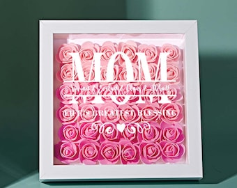 Könnte beinhalten: Weißer Rahmen mit einer Glasfront, gefüllt mit künstlichen Rosen in Rosa und Weiß. Das Wort "MOM" ist in Weiß geschrieben, darunter der Text "My Greatest Blessing".